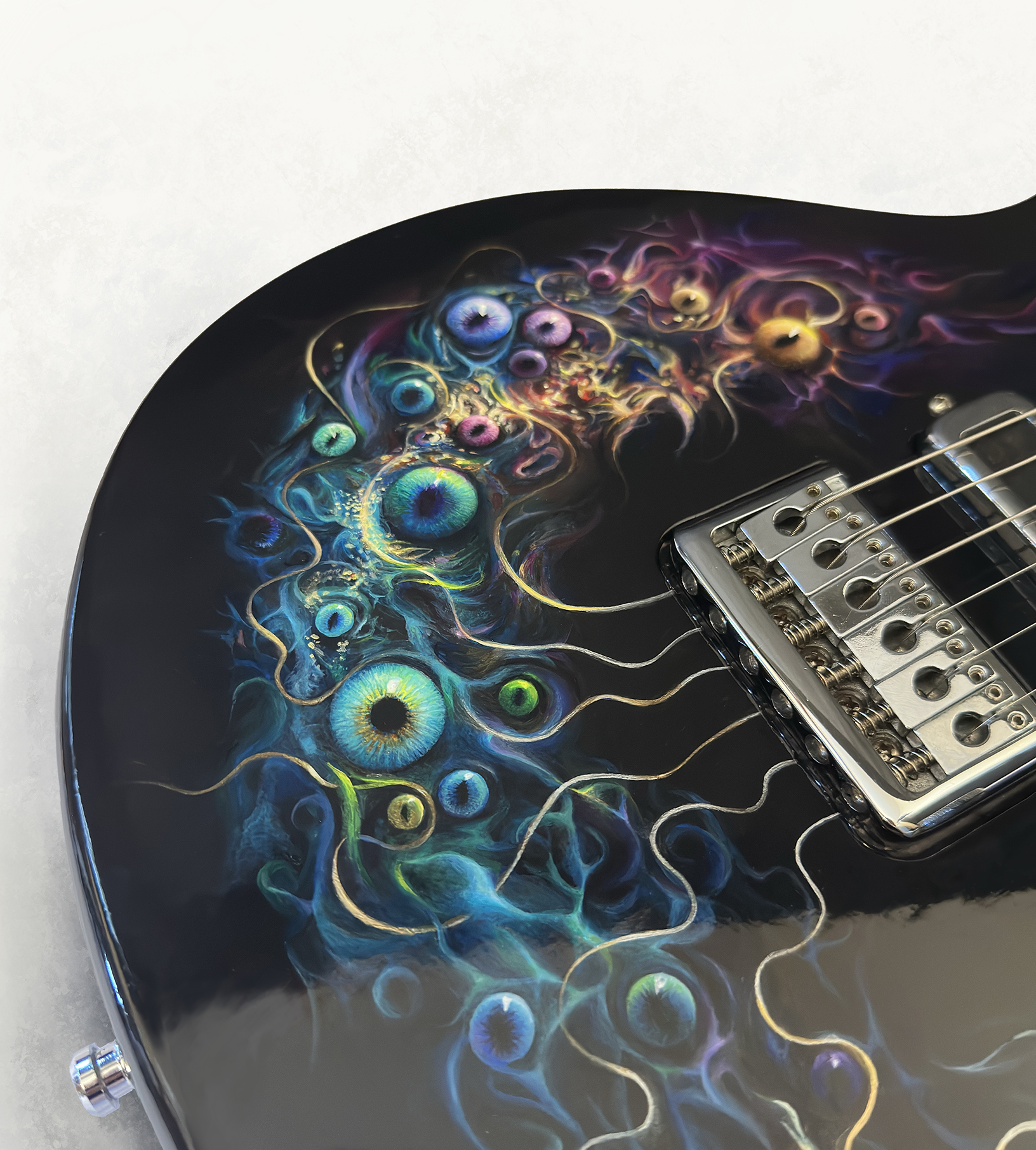 Close detail of eye-like forms and flowing blue colour painted around the guitar bridge.