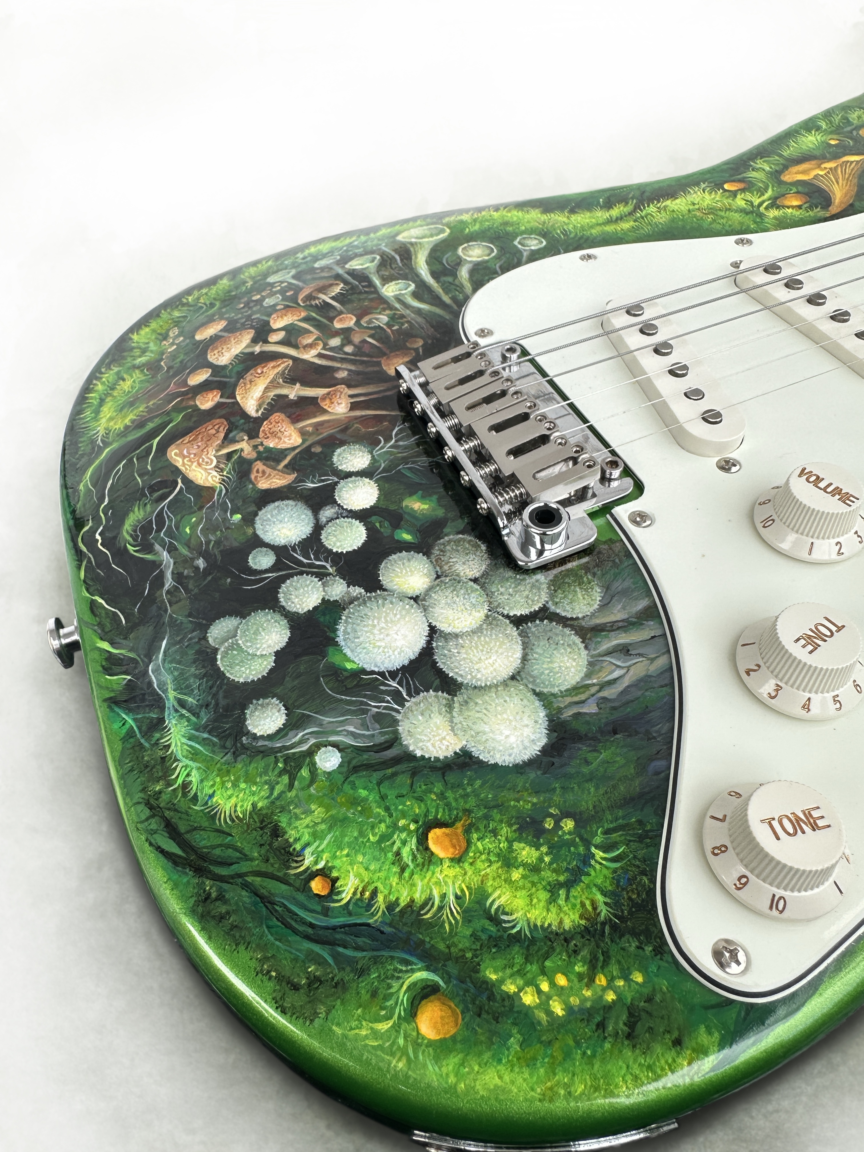 Macro view of hand-painted mushrooms, moss and pale spherical forms beside the bridge of a green guitar.