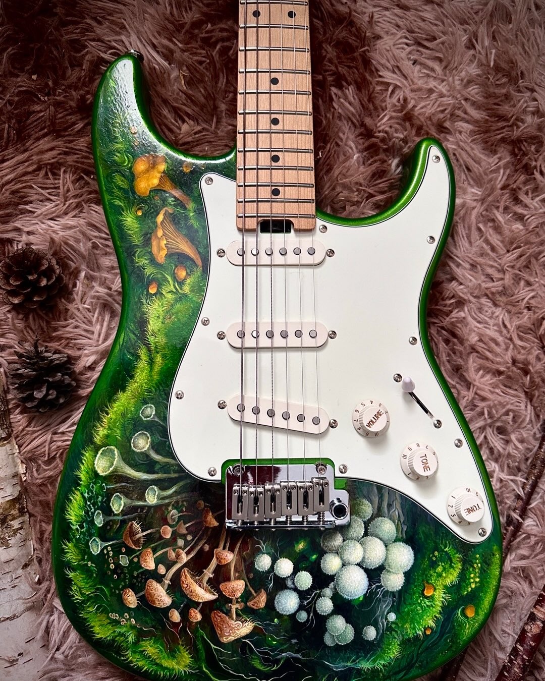Green electric guitar painted with a detailed woodland of mushrooms, moss and pale spherical forms.