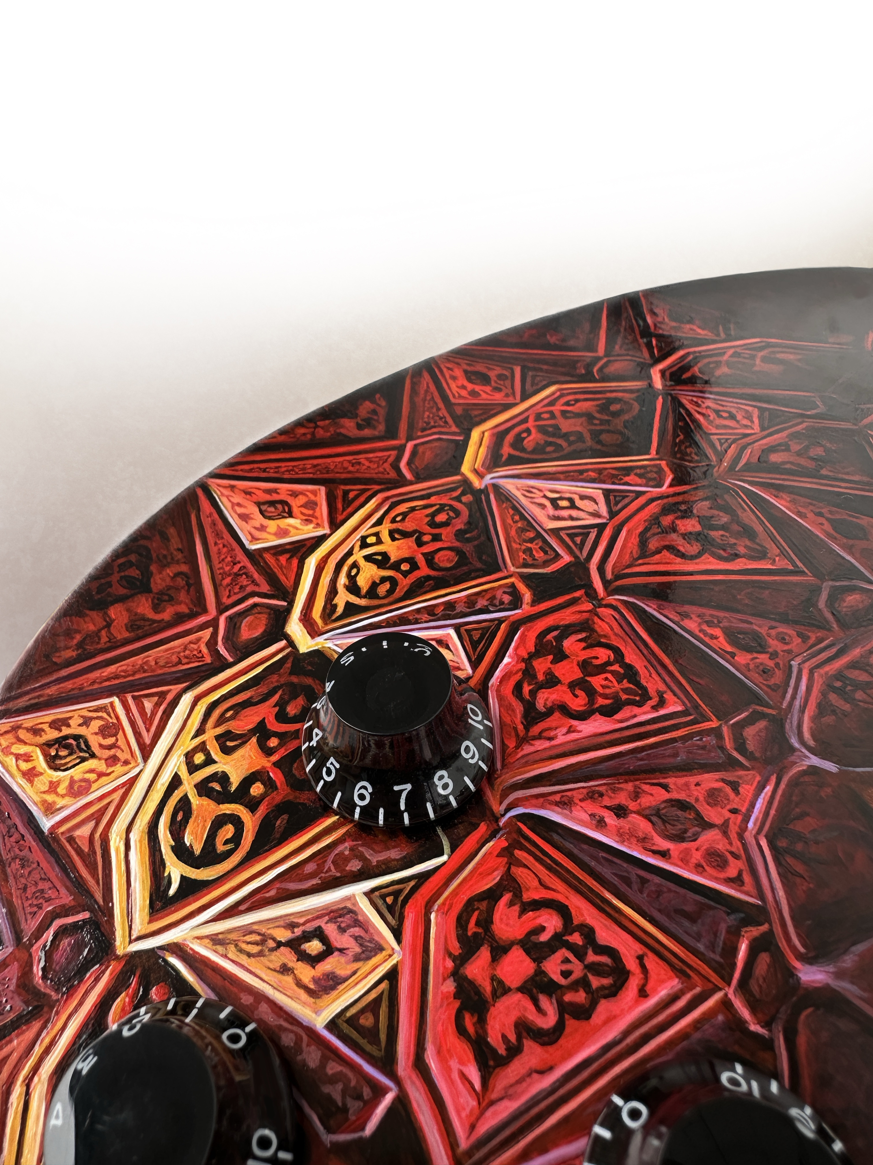 Close view of red, orange and black geometric painting around the controls of an electric guitar.
