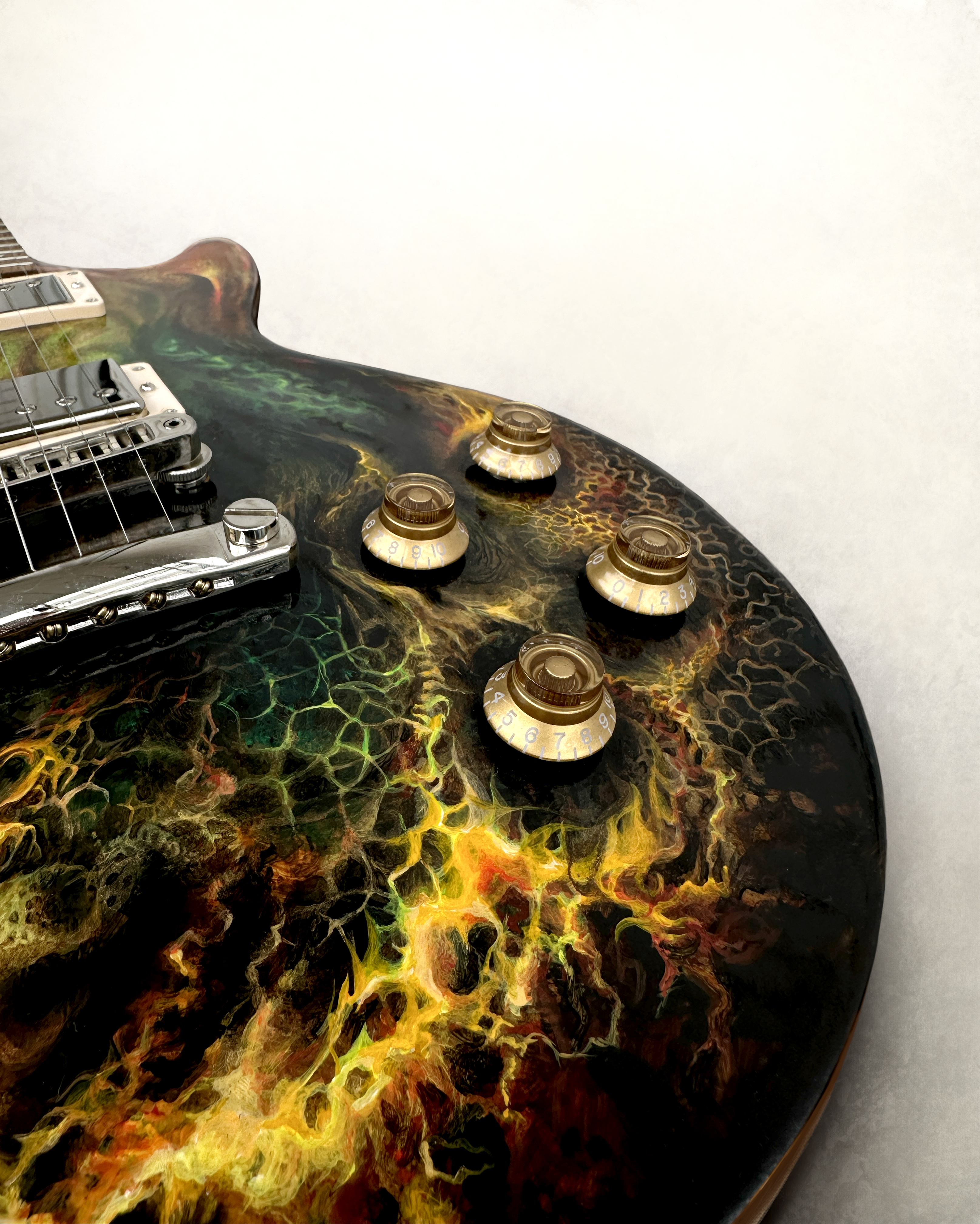 Macro view of branching gold, green and red colour around the controls of a dark electric guitar.
