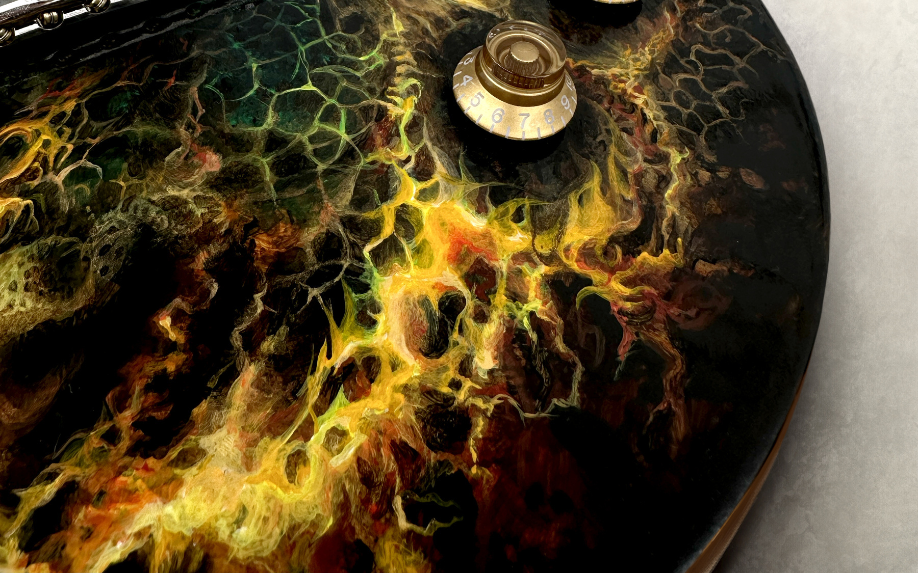 Close abstract view of gold and green painting flowing over a dark electric guitar.