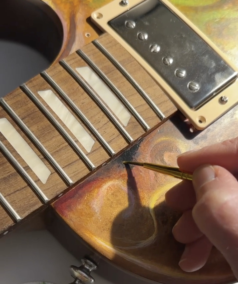 Sasha painting fine details by hand on a guitar body.