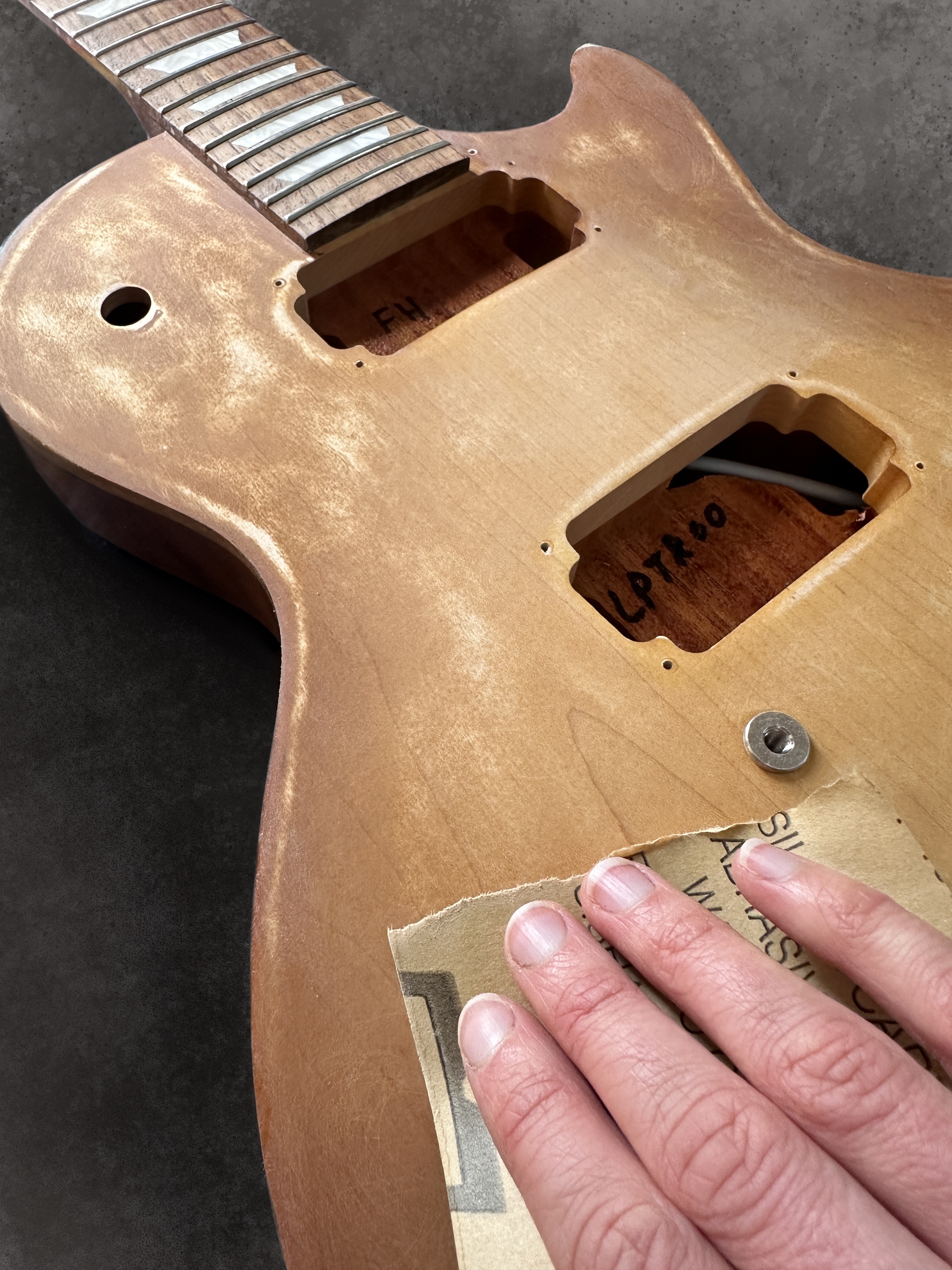 Hands preparing the surface of a guitar body for painting.