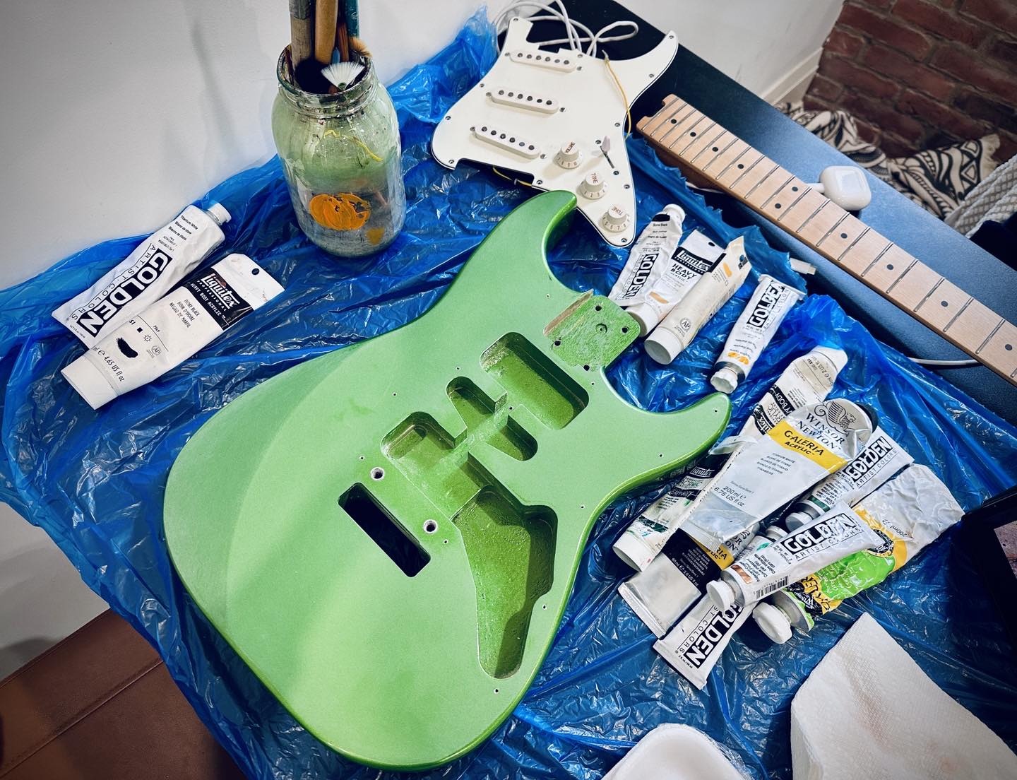Unpainted green guitar body, hardware and tools arranged on a studio worktable.